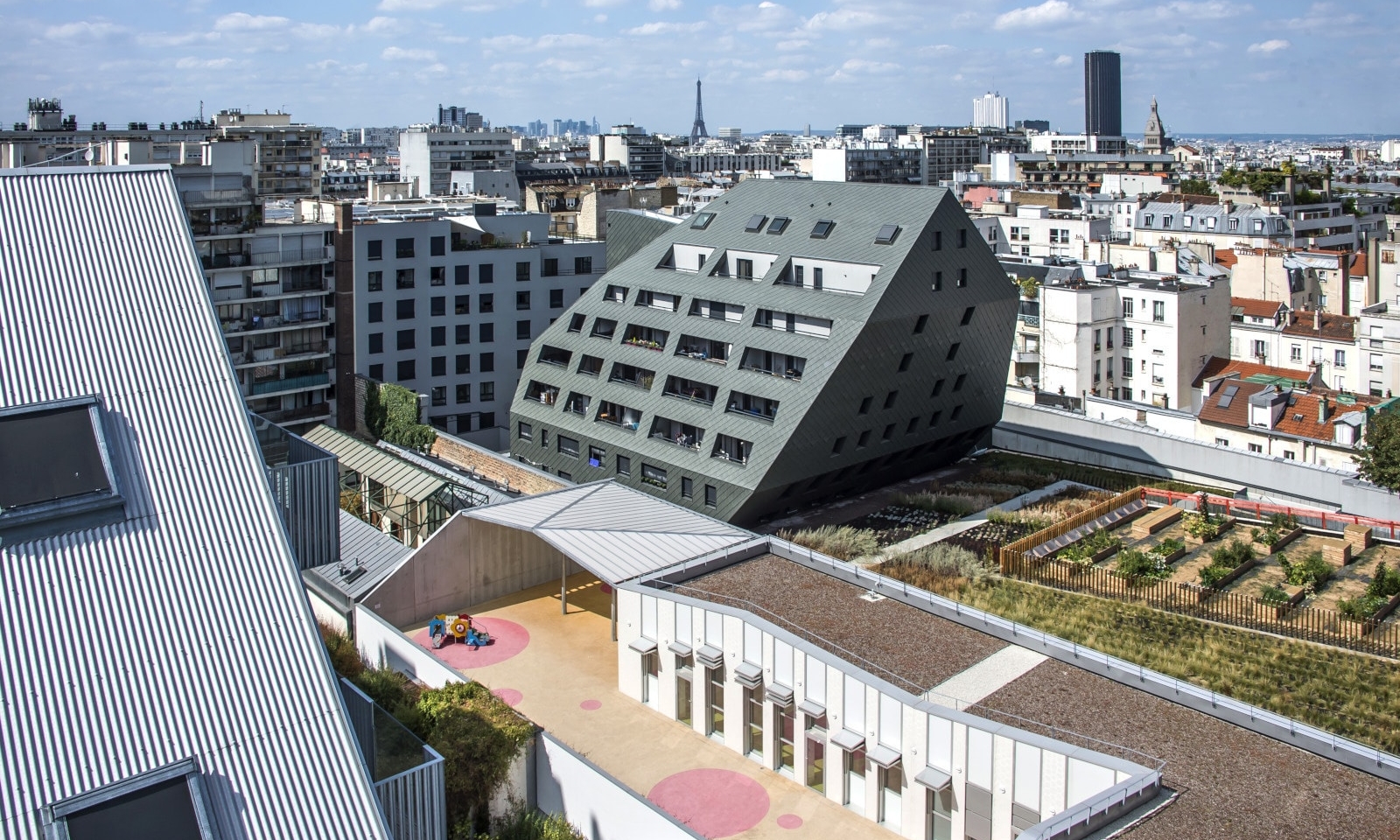 Vue panoramique du projet immobilier dans son environnement urbain parisien, avec bâtiments contemporains, toitures végétalisées et skyline de Paris en arrière-plan.